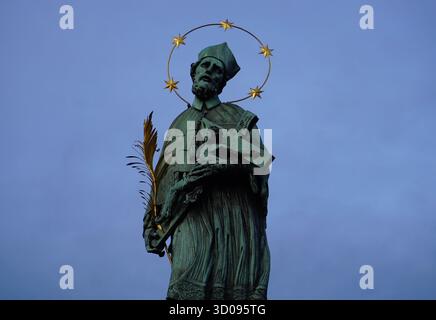 Nahaufnahme Porträt der Statue des heiligen Johannes von Nepomuk mit einem goldenen Halo auf der Karlsbrücke, Prag, Tschechische Republik, vor einem bewölkten Abendhimmel Stockfoto