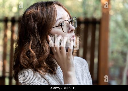 Eine junge rothaarige Frau, die telefoniert und draußen geschäftlich anruft Stockfoto