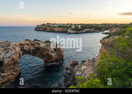 Goldene Stunde in Cala Santanyi, Mallorca, mit natürlichem Felsbogen, der aus dem Meer ragt. Malerische Mittelmeerküste in warmen Sonnenuntergangstönen. Stockfoto