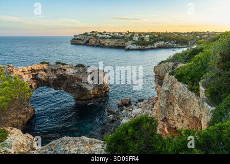 Majestätischer Steinbogen im Meer bei Cala Santanyí, Mallorca, Spanien bei Sonnenuntergang. Ruhige Meereslandschaft mit leuchtendem Himmel und Felsformationen an der Küste. Stockfoto