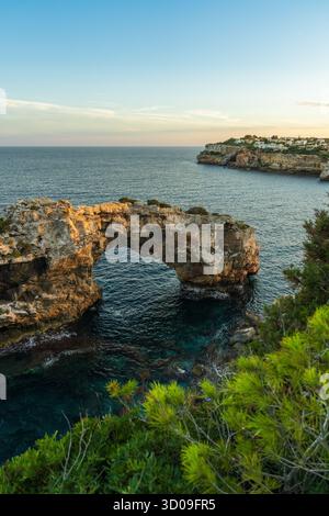 Blick auf den felsigen Meeresbogen bei Sonnenuntergang in Cala Santanyí, Mallorca. Warmes Licht reflektiert das ruhige Wasser und die natürlichen Klippen der Mittelmeerküste. Stockfoto