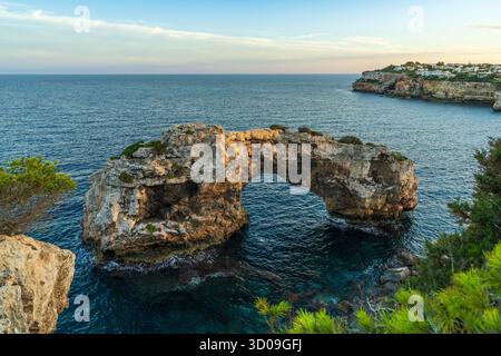 Natursteinbogen im Meer bei Cala Santanyi, Mallorca, glühend im goldenen Sonnenuntergang. Friedliche mediterrane Küstenszene mit dramatischem Rock-Format Stockfoto