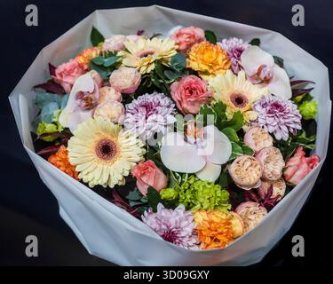 Ein luxuriöser und farbenfroher Blumenstrauß mit einer Mischung aus Rosen, Gerbera-Gänseblümchen, Orchideen und Chrysanthemen, eingewickelt in weißes Papier aus der neill-Straße Stockfoto