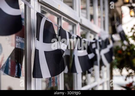 Bunting mit Flaggen von Cornwall hängen als Dekoration vor einem Pub-Fenster mit Aufklebern von British Union Flags, Cornwall, UK, Europa Stockfoto