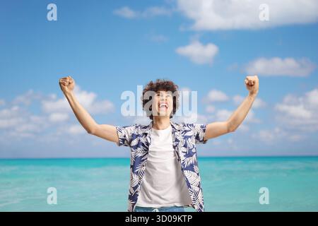 Ein überfröhlicher junger Mann in einem Sommerurlaub, der vor blauem Himmel und Meer glücklich ist Stockfoto