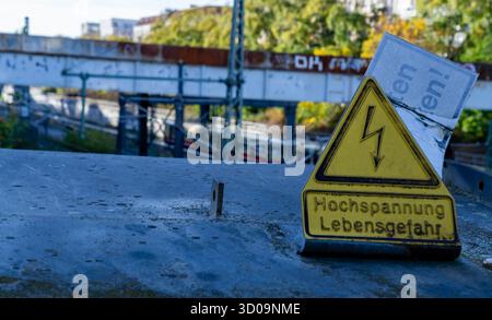 Deutsches dreieckiges gelbes Warnschild „Hochspannung Lebensgefahr“ auf einer Eisenbahnbrücke in Berlin Prenzlauer Berg. Stockfoto