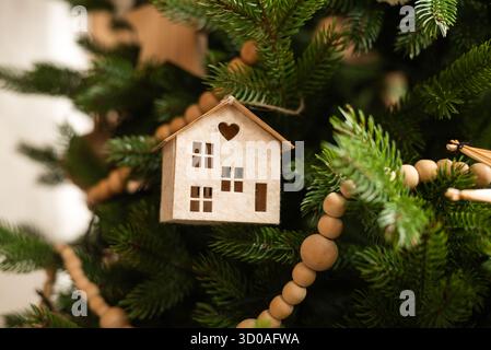 Ein bezauberndes hölzernes Miniaturhaus hängt an einem Weihnachtsbaum Stockfoto