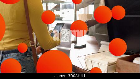 Mit Smartphone-Frau mit gelbem Oberteil, das QR-Code-Schild am Cafeteschalter mit Kartenleser scannt Stockfoto