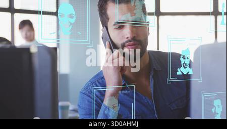 Sprechen auf Smartphone Nahöstlicher Mann, der Monitore auf dem Schreibtisch mit Erkennungsüberlagerungen ansieht Stockfoto