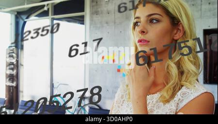 Stehende Frau, die im Büro mit Fahrrad an Akzentwand, Haftnotizen und numerischen Überlagerungen blickt Stockfoto