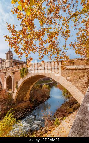 Herbst und Laub in Rom. Rote, orangene und gelbe Platanen auf der Tiber-Insel mit der alten römischen Brücke im historischen Zentrum der Stadt Stockfoto