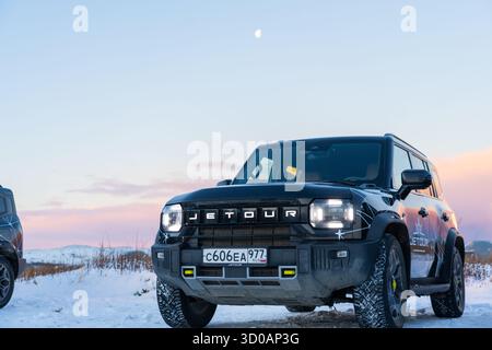 Murmansk, Russland - 13. Dezember 2024: Nahaufnahme des SUV Jetour T2 unter einem Halbmond in der Dämmerung. Nahaufnahme des schwarzen Jetour T bei niedrigem Winkel Stockfoto