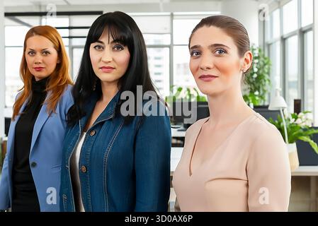 Drei Frauen in Geschäftskleidung posieren für ein Foto. Die Frauen tragen blaue und braune Outfits. Die Szene ist professionell und ernst Stockfoto