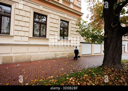 Tarnow, Polen - 10. Oktober 2025: Nonne mit Tasche geht auf dem Kopfsteinpflaster neben einer cremefarbenen Fassade. Stockfoto