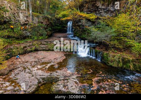 Wanderer ruht an einem Wasserfall, umgeben von Herbstlaub in einem walisischen Wald Stockfoto