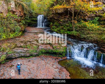 Wanderer mit Kamera und Blick auf einen kaskadierenden Wasserfall in einem walisischen Wald Stockfoto