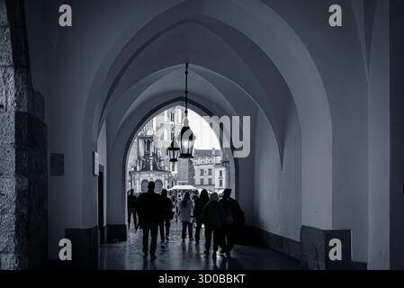 Schwarzweiß-Foto von Menschen, die durch die gewölbten Bögen der Tuchhalle (Sukiennice) in der Krakauer Altstadt spazieren. Aufgenommen am 11. Oktober 2025 Stockfoto