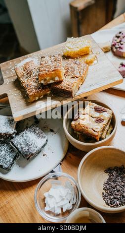 Ein Tisch mit verschiedenen Desserts, einschließlich Brownies, Keksen und Kuchen. Die Desserts sind auf einem Holzbrett und in Schüsseln angeordnet. Der Tisch ist eingestellt Stockfoto