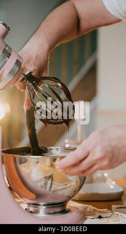 Eine Person macht ein Dessert in einem rosa Mixer. Das Dessert ist ein Schokoladenkuchen. Die Person mischt die Zutaten mit einem Schneebesen Stockfoto