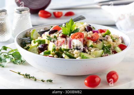 Nahaufnahme einer Schüssel mit israelischem Couscous-Salat mit Zutaten überall. Stockfoto