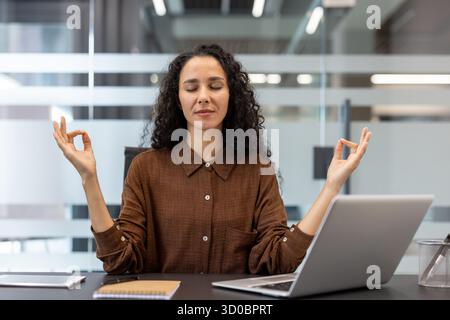 Professionelle Geschäftsfrau meditiert an ihrem Schreibtisch, übt Stress und Achtsamkeit während einer Pause, findet inneren Frieden und fördert geistiges Wohlbefinden Stockfoto