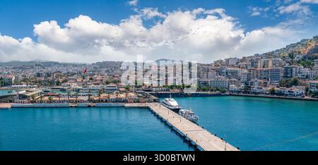 Kusadasi, Aydin, Türkei - 23. August 2025: Panoramablick auf den Kusadasi Kreuzfahrtschiffpier und den geschäftigen Handelshafen mit der Stadt auf dem Stockfoto