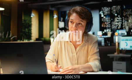 Frau, die an einem Remote-Webinar vom Schreibtisch aus mit Laptop und Headset teilnimmt und mit den Teilnehmern interagiert. Person, die Augenkontakt hält und Ideen in einem Chat austauscht, der das Networking fördert. Kamera A.. Stockfoto