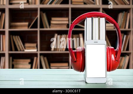 Modernes Mobiltelefon, Kopfhörer und Bücher auf dem Tisch in der Bibliothek. Hörbuchkonzept Stockfoto