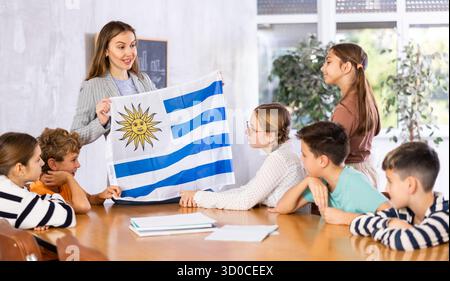 Lehrer, der einer Gruppe von Schulkindern die Uruguay-Flagge zeigt Stockfoto
