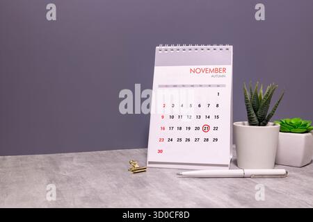 Kalender für November 21: Monatsname in englischer Sprache, Nummer 21, Birkenzweig mit einem gelben Blatt, gefallene Birkenblätter auf einem Holztisch, grauer Rücken Stockfoto