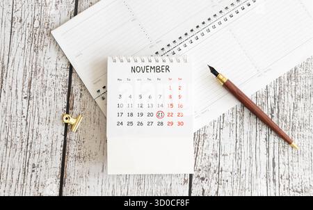 Kalender für November 21: Monatsname in englischer Sprache, Nummer 21, Birkenzweig mit einem gelben Blatt, gefallene Birkenblätter auf einem Holztisch, grauer Rücken Stockfoto