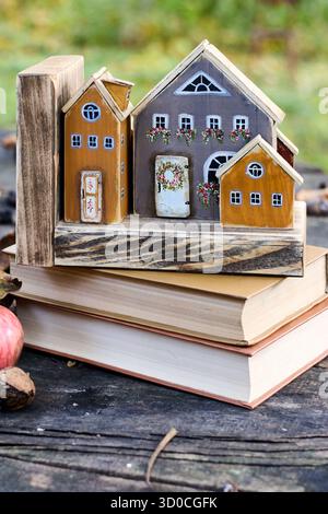 Charmante Miniatur-Holzhäuser sitzen auf gestapelten Büchern auf einer rustikalen Holzoberfläche, und ein Apfel und Walnüsse sorgen für die gemütliche Atmosphäre. Stockfoto