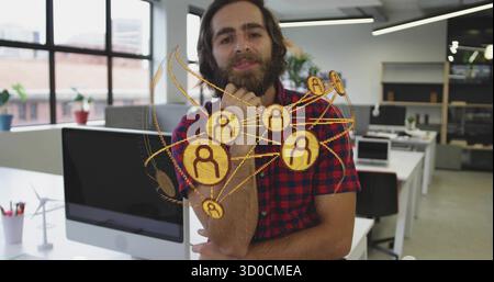 Bärtiger Mann, der kariertes Hemd trägt, das Kinn auf der Faust am Bürotisch aufliegt, mit Windturbine Stockfoto