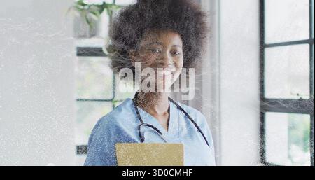 Krankenschwester mit Stethoskop mit gelbem Ordner, lächelnd in der Klinik an verglasten Fenstern Stockfoto