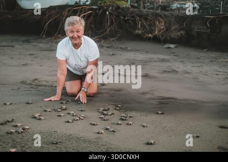 Portrait ältere grauhaarige weibliche Freiwillige, die Baby-Meeresschildkröten am Strand freilässt Stockfoto
