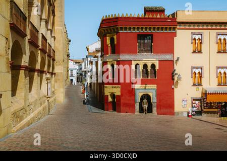 Historische Straße in Cordoba, Spanien, mit traditioneller andalusischer Architektur mit leuchtenden roten und gelben Gebäuden, verzierten Fenstern und einer Person Stockfoto