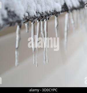 Nahaufnahme von Eiszapfen, die im Winter von einem schneebedeckten schwarzen Dach hängen. Stockfoto