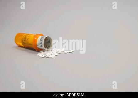 Verschreibungspflichtige Pillen wurden aus einem Behälter mit einem 100-Dollar-Schein auf den Tisch geschüttet. Eine Ebene Ansicht auf grauem Hintergrund. Stockfoto