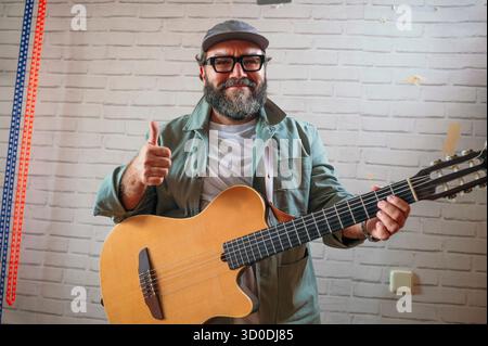 Ein Mann, der die Daumen hoch hält, während er die Akustikgitarre hält. Stockfoto