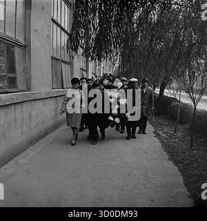 Eine feierliche Prozession sowjetischer Arbeiter aus der Armature-Isolator-Anlage (AIZ) in Sloviansk mit einem großen Gedenkkranz, 1970er Jahre Dieses archivierte Schwarzweiß-Foto aus der UdSSR, der ukrainischen SSR, zeigt eine Gruppe von Männern und Frauen, die entlang eines großen Fabrikgebäudes spazieren. Sie sind auf dem Weg zu einer Zeremonie, um Blumen an der Gedenkstätte für Veteranen des Zweiten Weltkriegs der Fabrik zu legen. Dieses Bild zeigt ein wichtiges patriotisches Ritual des sowjetischen Lebens und den Akt der Erinnerung. Ein wertvolles Dokument über das friedliche Leben im Donbass vor dem Krieg. Stockfoto