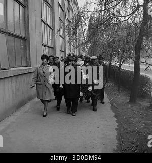 Eine feierliche Prozession sowjetischer Arbeiter aus der Armature-Isolator-Anlage (AIZ) in Sloviansk mit einem großen Gedenkkranz, 1970er Jahre Dieses archivierte Schwarzweiß-Foto aus der UdSSR, der ukrainischen SSR, zeigt eine Gruppe von Männern und Frauen, die entlang eines großen Fabrikgebäudes spazieren. Sie sind auf dem Weg zu einer Zeremonie, um Blumen an der Gedenkstätte für Veteranen des Zweiten Weltkriegs der Fabrik zu legen. Dieses Bild zeigt ein wichtiges patriotisches Ritual des sowjetischen Lebens und den Akt der Erinnerung. Ein wertvolles Dokument über das friedliche Leben im Donbass vor dem Krieg. Stockfoto