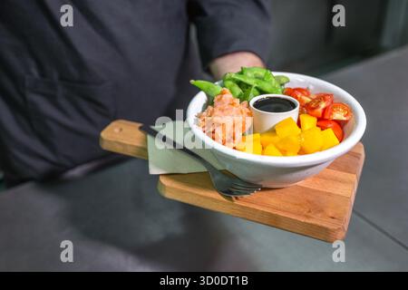 Nicht wiedererkennbarer Koch zeigt frisch zubereitete bunte Poke Bowl mit Lachs in der Restaurantküche Stockfoto