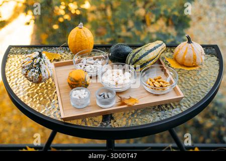 Flatlay von Herbstkürzeln und verschiedenen Beilagen in Glasschalen, die auf einem Holztablett über Herbstlaub angeordnet sind. Funktionelle Ernährung in der Natur Stockfoto