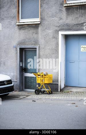 Ein gelber Lieferwagen der Deutschen Post steht vor einer grauen Fassade zwischen einer Haustür und einem großen, hellblauen Garagentor, Wuppertal Stockfoto