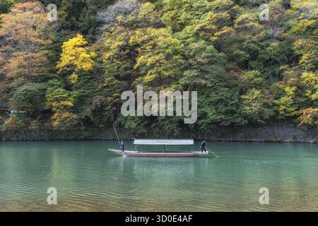 Bootsfahrt auf dem Katsura Fluss während der Herbstsaison. Bootsführer benutzen lange Bambusstangen zum Lenken. Aufgenommen in Arashiyama, Kyoto, Japan Stockfoto