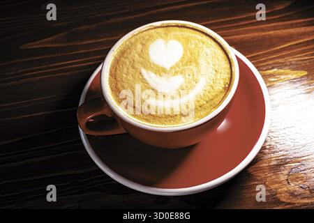 Rote Tasse Latte Coffee mit Schaumkunstwerk oben, halb dunkel über dem Holztisch Stockfoto