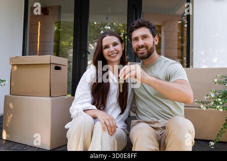 Glückliches Paar, das am Eingang ihrer neuen Unterkunft sitzt und zufrieden aussieht Stockfoto