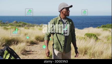 Wandermann mit Mütze und Hemd entlang des Küstengraslandwegs, mit AR-Symbolen und Rucksack Stockfoto