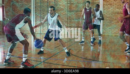 Dribbelsportler, der sich auf dem Hartholzplatz in einem Fitnessstudio aus Ziegelstein entzieht, mit blau-weißem Basketball Stockfoto