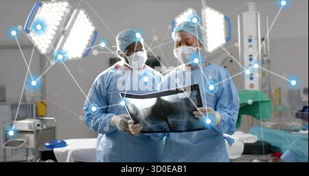 Zwei Chirurgen mit Peelings, die Röntgenaufnahmen in der Brust im OP überprüfen, mit Operationslampen Stockfoto